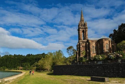 Historic stone chapel with spire overlooking green lake at Villa Várzea guesthouse in Várzea, Portugal