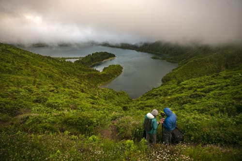Hikers overlooking lakes at Várzea, Portugal, lush green hills and misty mountains in background