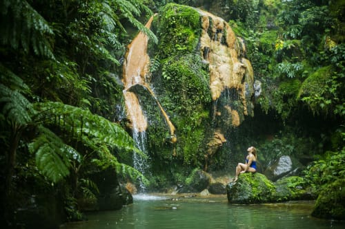 Woman relaxing by emerald pool at Villa Várzea waterfall in Várzea, Portugal, surrounded by lush green forest