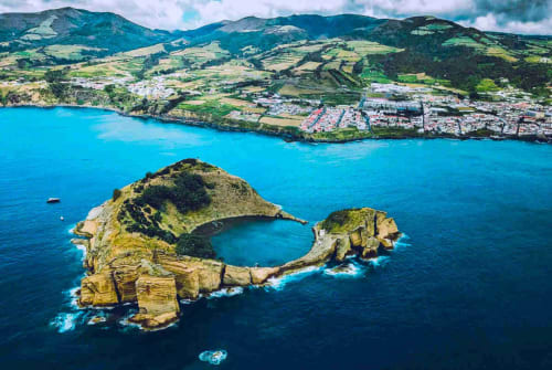Aerial view of Manta Ray rock formation near Várzea, Azores with turquoise ocean and coastal town backdrop.
