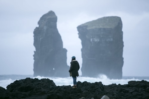 Traveler standing on rocky shore facing dramatic sea stacks near Várzea, Portugal