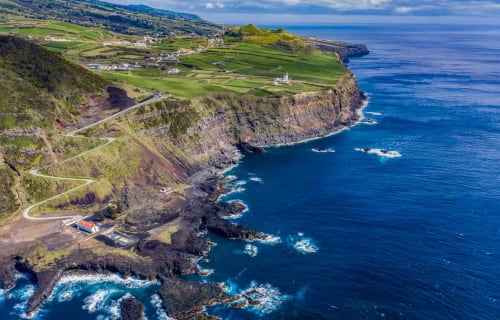 Aerial view of Villa Várzea cliffside location in Portugal with green fields, winding road, and blue Atlantic Ocean coast