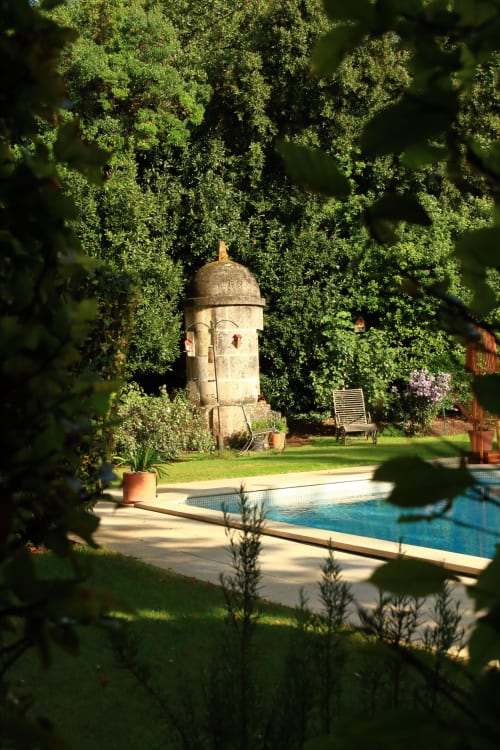 Tour de pierre couverte de lierre au Logis des Tourelles à Cognac, avec piscine et chaises longues visibles