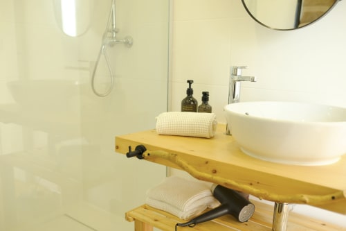 Modern bathroom at Villa Várzea with wooden vanity, white round sink, rolled towels, and shower in Black Cabin room