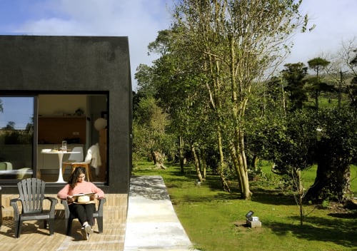 Guest relaxing on patio of Black Cabin at Villa Várzea with garden views and tree-lined grounds in Várzea, Portugal