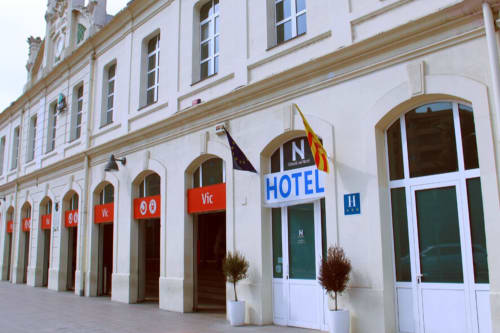 Entrada del hotel Estació del Nord en Vic, Barcelona con fachada blanca, puertas arqueadas, toldos rojos y macetas