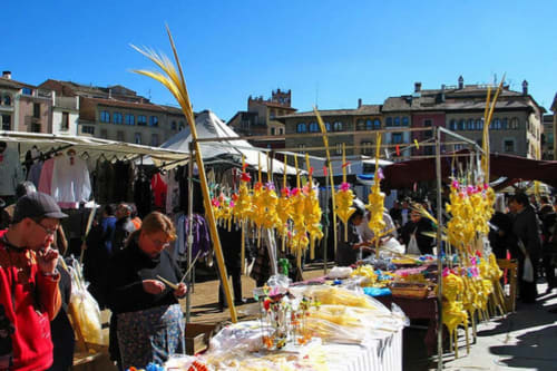Mercat a l'aire lliure a Vic, Barcelona amb flors grogues, parades i arquitectura històrica sota un cel blau clar