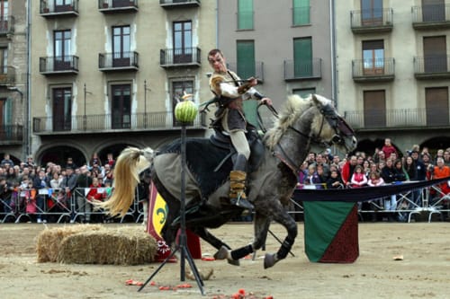 Espectacle de justa medieval a la plaça de Vic amb cavall, cavaller i espectadors prop d'edificis històrics