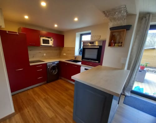 Cuisine moderne de La Maison De Fleurat avec armoires rouges, îlot, électroménagers et parquet