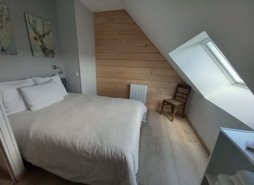 Chambre cosy sous les combles à La Maison De Fleurat à Domeyrot avec literie blanche, poutres en bois, fenêtres de toit et mobilier épuré.