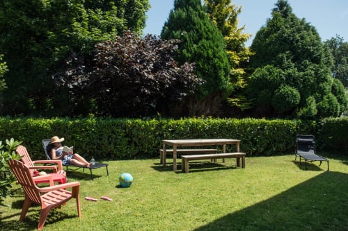 Sunny garden at Au Gîte d'Isigny cottage with red chairs, picnic table, and evergreen hedges in Isigny-sur-Mer