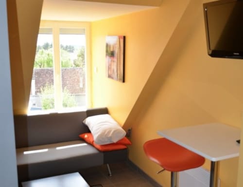 Chambre jaune vif à l'hôtel Mape à Dampierre-en-Burly, avec fenêtre, banc noir, chaise rouge et télévision