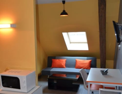 Chambre moderne du Mape Hotel à Dampierre en Burly avec canapé gris, coussins orange, puits de lumière et mobilier contemporain