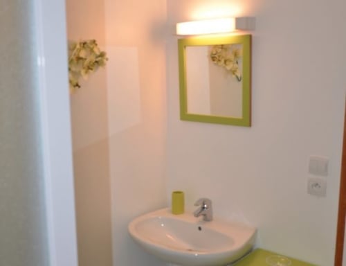 Salle de bains moderne de l'Hôtel Mape à Dampierre en Burly avec lavabo blanc, miroir à cadre vert et détails muraux décoratifs