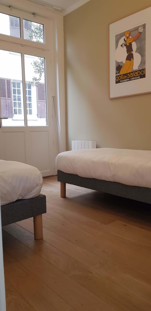 Deux lits jumeaux aux draps blancs dans une chambre lumineuse des Cabines à Houlgate, avec grandes fenêtres et style vintage