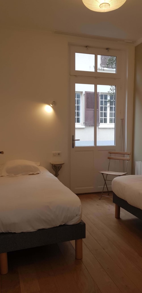 Chambre lumineuse à l'hôtel Les Cabines à Houlgate avec deux lits, portes vitrées ouvertes sur le jardin et équipements modernes