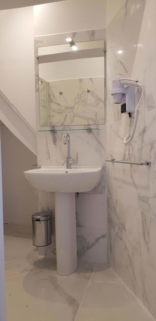 Salle de bain moderne de l'hôtel Les Cabines à Houlgate avec murs en marbre, lavabo sur piédestal, miroir et équipements muraux