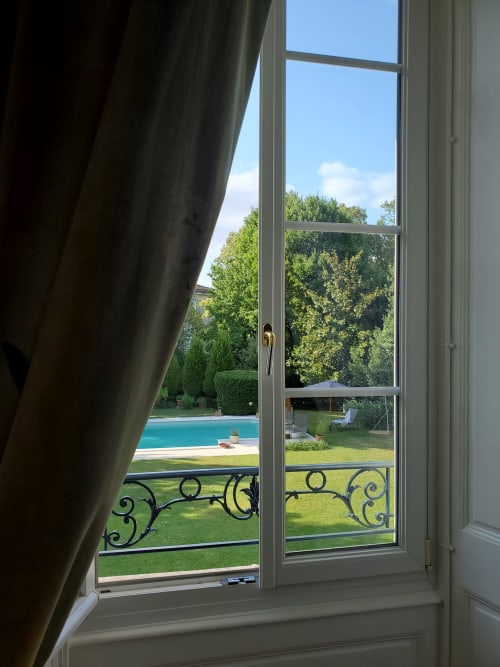 Vue de la chambre Bassac au Logis des Tourelles à Cognac : jardin, piscine et parc paysagé à travers les vitres