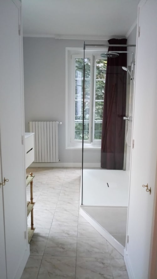 Salle de bain moderne avec douche vitrée, radiateur blanc et vue sur la fenêtre aux Logis des Tourelles, Cognac
