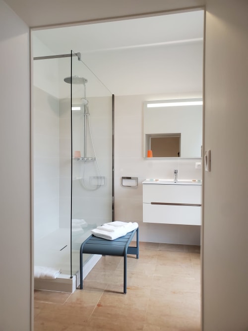 Salle de bains moderne avec douche vitrée, vasque blanche et banquette noire au Logis des Tourelles à Cognac