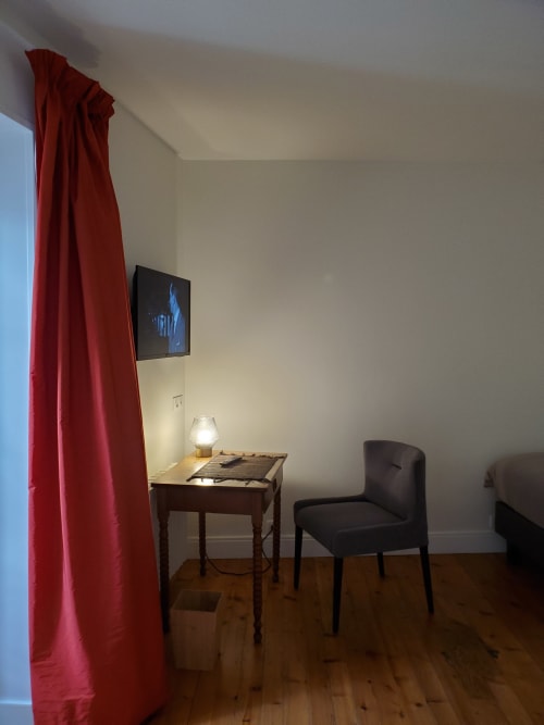 Chambre Salignac au Logis des Tourelles, Cognac : bureau avec lampe, chaise noire, TV murale, rideaux rouges, parquet