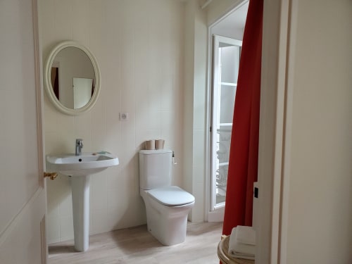 Salle de bains moderne au Logis des Tourelles à Cognac avec lavabo sur pied, toilettes, miroir ovale et rideau rouge