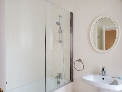 Salle de bain moderne du Logis des Tourelles à Cognac avec douche vitrée, lavabo blanc, miroir rond et accessoires chromés