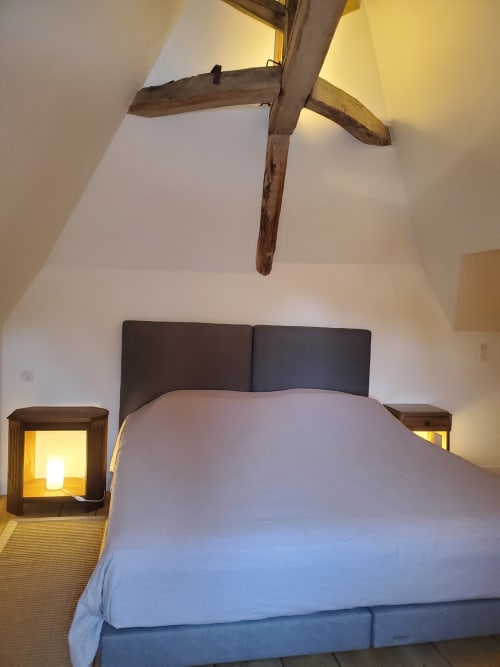 Gezellige slaapkamer in Logis des Tourelles in Cognac met zichtbare houten balken, donker hoofdbord, wit beddengoed en warm licht