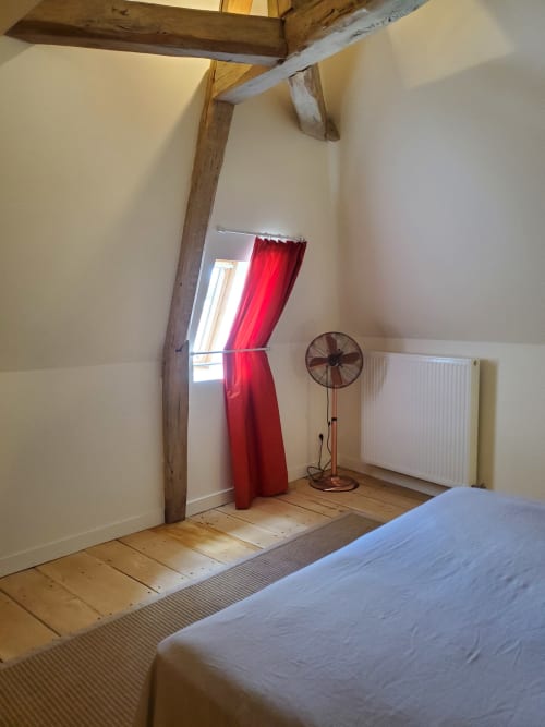 Slaapkamer van het appartement Bouteville met blootgestelde houten balken, witte muren, houten vloeren en tuinzicht bij Logis des Tourelles