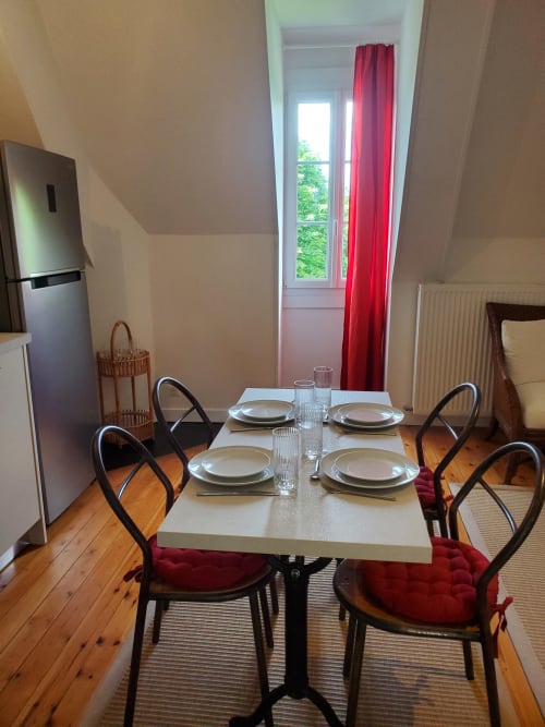 Eetkamer van het Cognac-appartement met tafel gedekt voor vier, zwarte stoelen, houten vloeren en tuinuitzicht door rode gordijnen