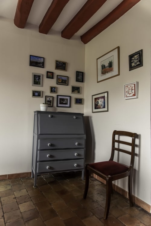 Chambre chaleureuse au refuge des Alpes mancelles avec commode noire, chaise en bois, galerie murale et poutres apparentes