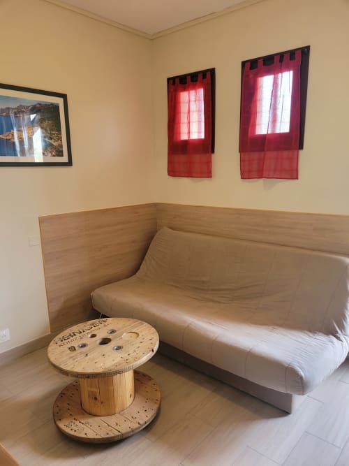Coin salon douillet avec canapé beige, table en bois et rideaux rouges dans un gîte corse avec vue sur mer