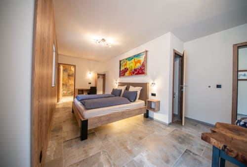 Chambre moderne à la Villa Valtin avec lit en bois, sols en pierre, œuvres d'art colorées et vues sur les montagnes