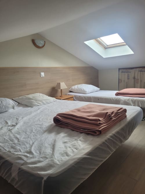Chambre mansardée avec deux lits, têtes de lit en bois, lucarne et vue sur la mer en Corse
