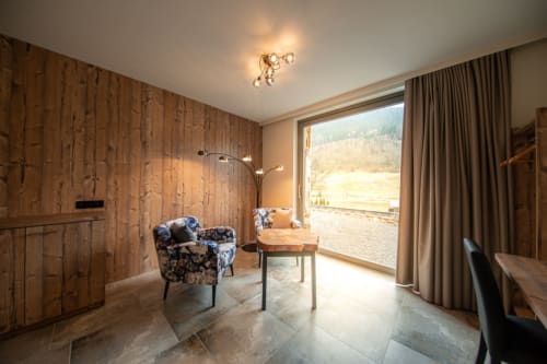 Chambre moderne à la Villa Valtin au Valtin avec mur en bois, fauteuil bleu à motifs et vue sur les montagnes depuis le balcon