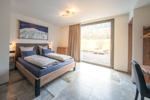 Chambre contemporaine à la Villa Valtin avec vue jardin, lit en bois, parure bleue et portes-fenêtres