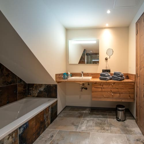 Salle de bain moderne de la Villa Valtin avec vasque en bois, miroir rétroéclairé, baignoire et carrelage en pierre