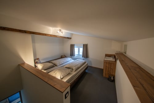 Spacieuse chambre loft à la Villa Valtin avec lit surélevé, poutres en bois, porte-fenêtre et vue sur le jardin au Valtin