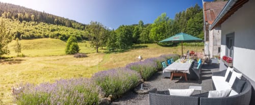 Patio du cottage Villa Valtin avec jardin de lavande, vue sur les montagnes, table à dîner, chaises longues et parasol turquoise au Valtin