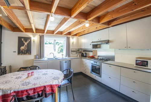 Cuisine de cottage moderne à la Villa Valtin avec armoires blanches, poutres en bois, table à manger et vue montagne
