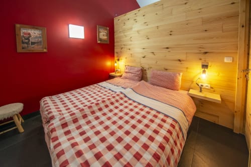 Chambre douillette à la Villa Valtin avec murs rouges, boiseries de sapin, linge à carreaux et ambiance chaleureuse au Valtin