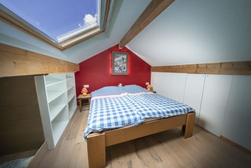 Chambre mansardée lumineuse à la maison d'hôtes Villa Valtin avec lit en bois, mur accent rouge, puits de lumière et rangements blancs au Valtin