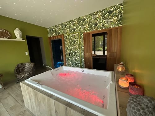 Baignoire de luxe aux lumières rouges dans l'élégante salle de spa de La Cour d'Hortense, avec murs verts et vue sur le jardin