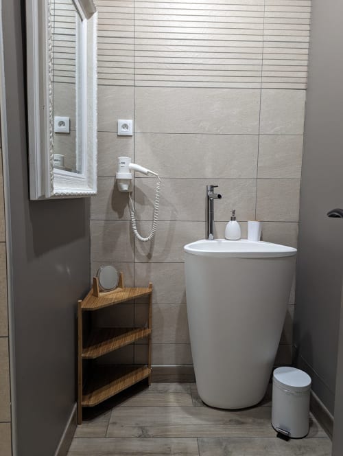 Lavabo moderne sur colonne avec étagère en bois et murs carrelés à La Cour d'Hortense