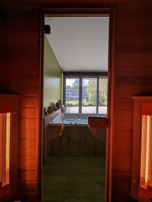 Entrée du spa La Cour d'Hortense avec bain à remous, lampes chauffantes et vue sur le jardin par portes vitrées