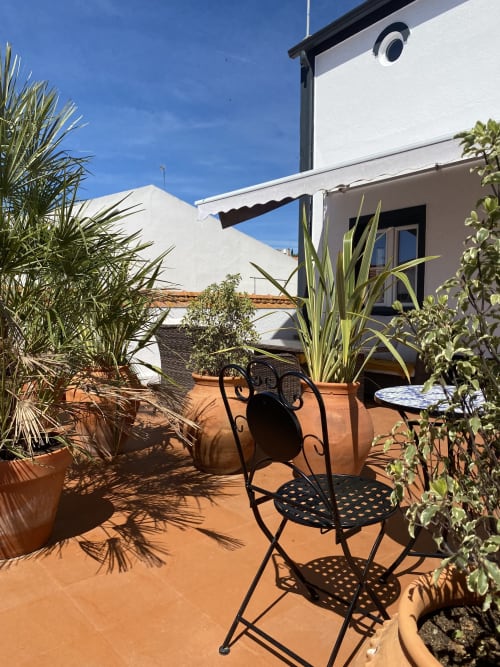 Terraço ensolarado na cobertura da pousada Patio Da Villa Coruche com cadeiras de bistró pretas, plantas em vasos e design moderno branco