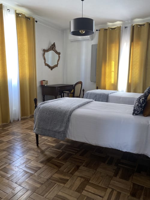 Elegant bedroom at Patio Da Villa guest house in Coruche with two beds, gold curtains, and parquet flooring