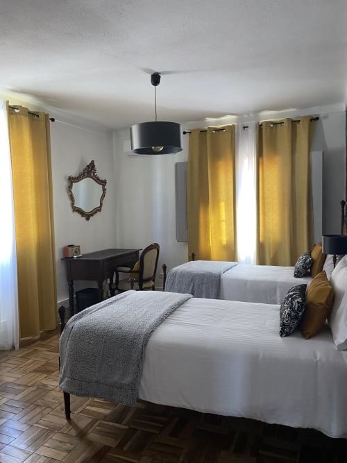 Modern bedroom at Patio Da Villa Coruche with twin beds, yellow curtains, pendant light, and dark wood desk