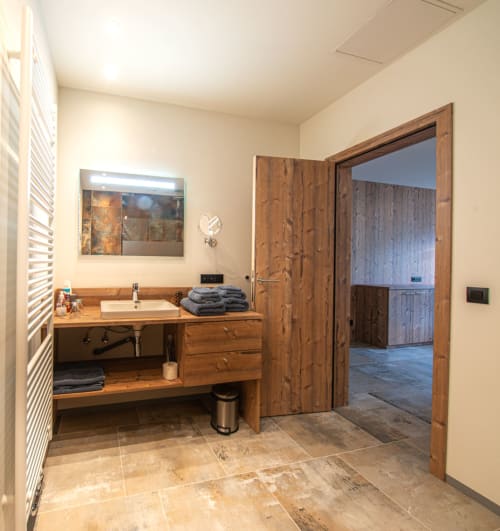 Salle de bain moderne à la Villa Valtin avec vasque en bois, vue montagne par les portes ouvertes et accès au balcon avec vue sur les montagnes au