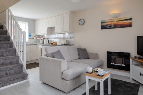 Cornish Holiday - 100 Hengar Manor. The open plan lounge with electric flame effect fire and smart TV, along with a view of the kitchen and the bottom of the stairs.